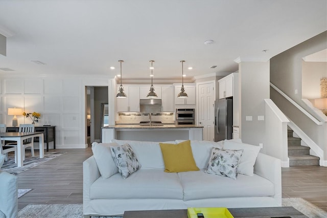 living room with wood-type flooring, crown molding, and sink