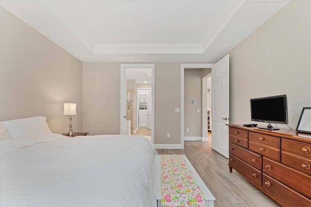 bedroom featuring light hardwood / wood-style floors, connected bathroom, and a tray ceiling