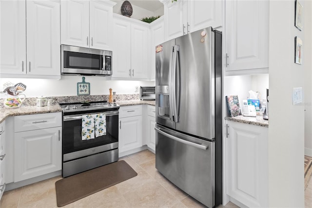 kitchen with light stone countertops, white cabinets, light tile patterned flooring, and appliances with stainless steel finishes