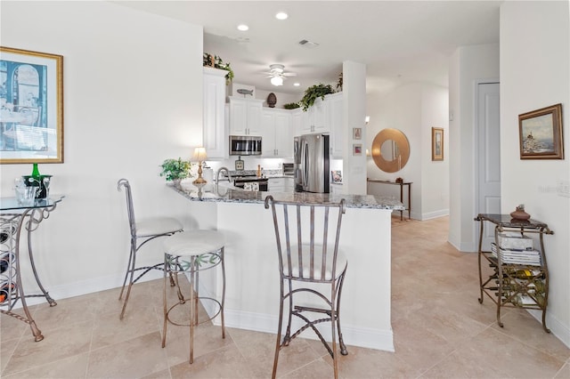 kitchen featuring white cabinets, appliances with stainless steel finishes, kitchen peninsula, and stone counters