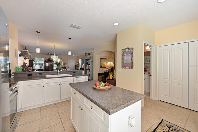 kitchen with pendant lighting, a center island, sink, stainless steel stove, and white cabinetry