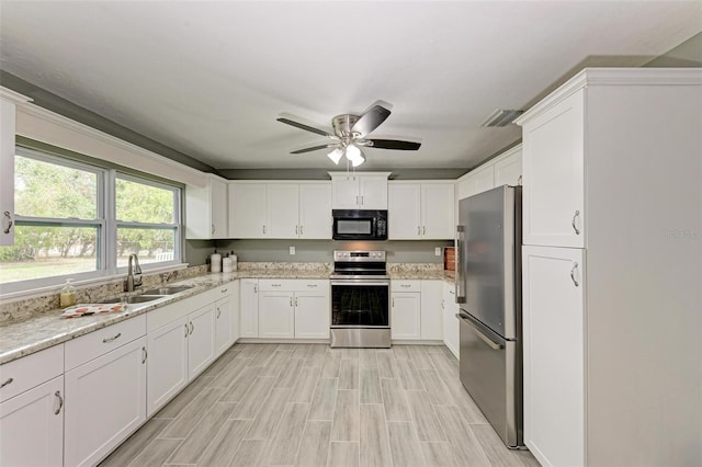 kitchen featuring light wood-type flooring, light stone counters, stainless steel appliances, sink, and white cabinets