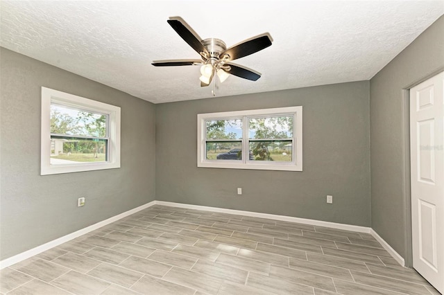 empty room featuring a wealth of natural light, ceiling fan, a textured ceiling, and light wood-type flooring