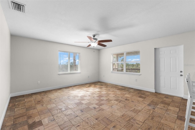 empty room featuring a textured ceiling, a wealth of natural light, and ceiling fan