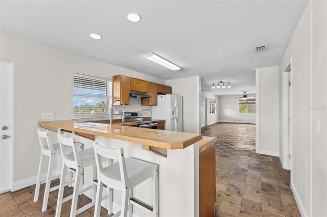 445 Horseshoe Loop Rd, Terra Ceia, FL 34250 - kitchen with white refrigerator with ice dispenser, electric range, under cabinet range hood, brown cabinets, and baseboards