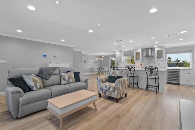 living room featuring crown molding, plenty of natural light, beverage cooler, and light hardwood / wood-style floors