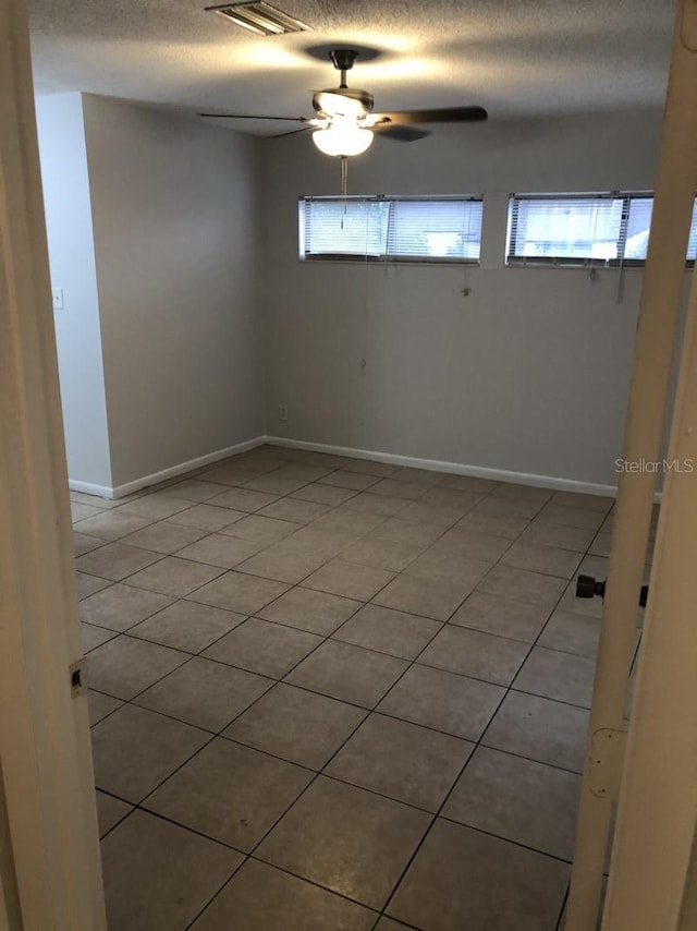 tiled spare room featuring plenty of natural light, ceiling fan, and a textured ceiling