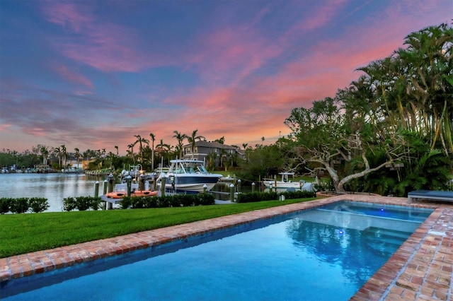 pool at dusk featuring a boat dock, a water view, and a yard