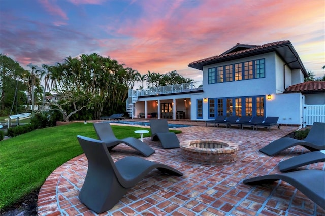 back house at dusk with a lawn, a patio area, and a fire pit