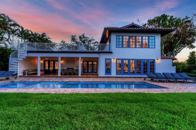 back house at dusk with outdoor lounge area, a patio area, a yard, and french doors