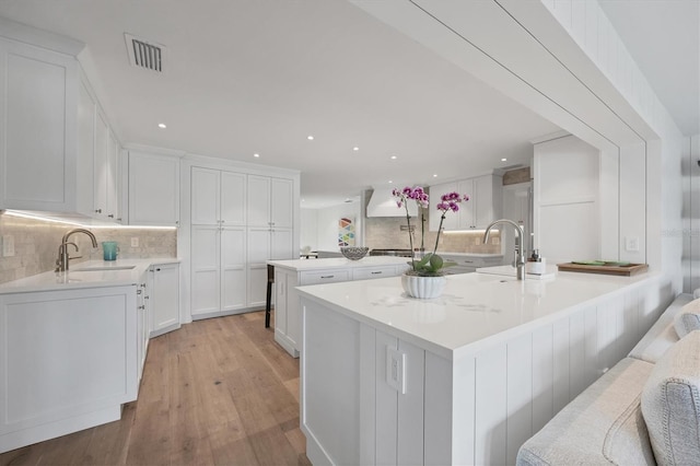 kitchen with kitchen peninsula, sink, white cabinets, a center island, and light hardwood / wood-style floors