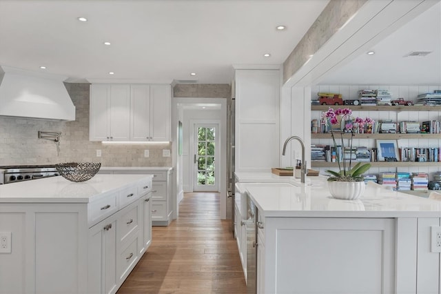 kitchen featuring a center island with sink, white cabinetry, light wood-type flooring, and custom range hood