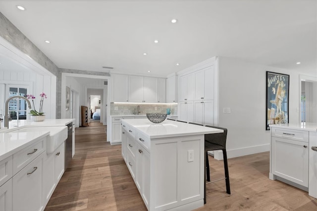 kitchen with stainless steel dishwasher, a kitchen island, white cabinetry, and light hardwood / wood-style flooring