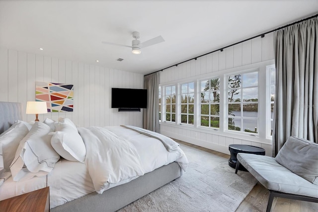 bedroom with ceiling fan, wood-type flooring, and wooden walls