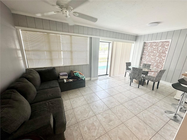 tiled living room featuring a textured ceiling, ceiling fan, wood walls, and crown molding