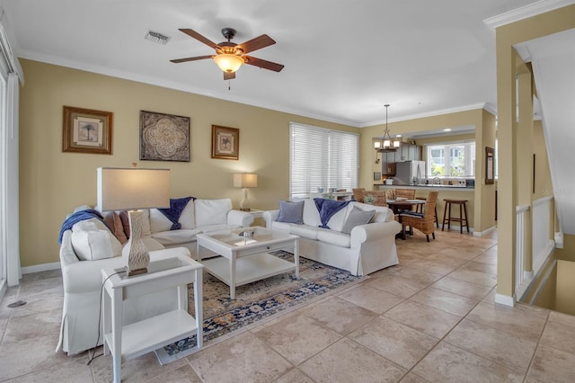 tiled living room with ceiling fan with notable chandelier and ornamental molding