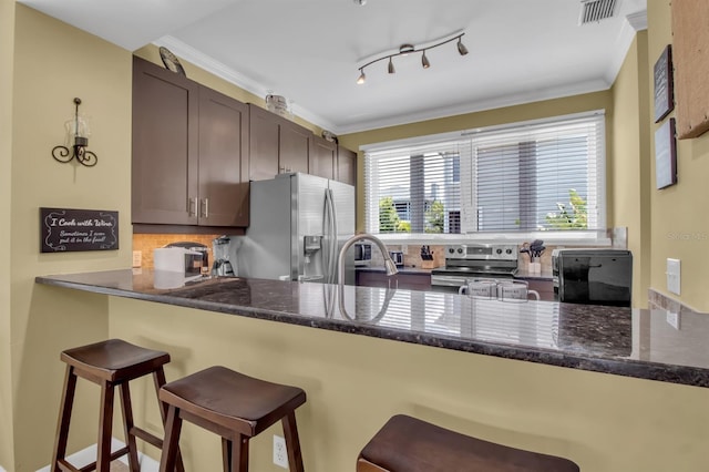 kitchen featuring dark brown cabinetry, stainless steel appliances, kitchen peninsula, crown molding, and a kitchen bar