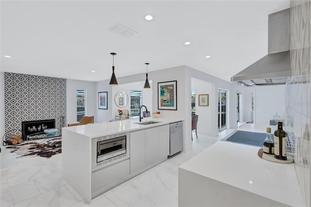 kitchen featuring sink, wall chimney exhaust hood, hanging light fixtures, an island with sink, and appliances with stainless steel finishes