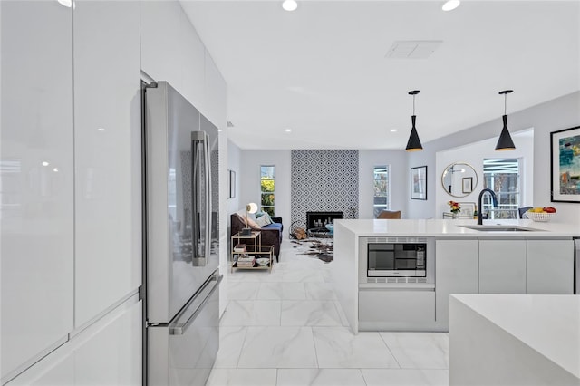 kitchen with stainless steel appliances, sink, white cabinets, hanging light fixtures, and a tiled fireplace