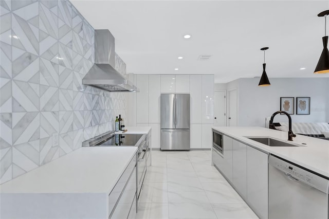 kitchen with sink, hanging light fixtures, wall chimney exhaust hood, white cabinetry, and stainless steel appliances