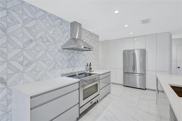 kitchen featuring wall chimney exhaust hood, white cabinetry, tile walls, and appliances with stainless steel finishes