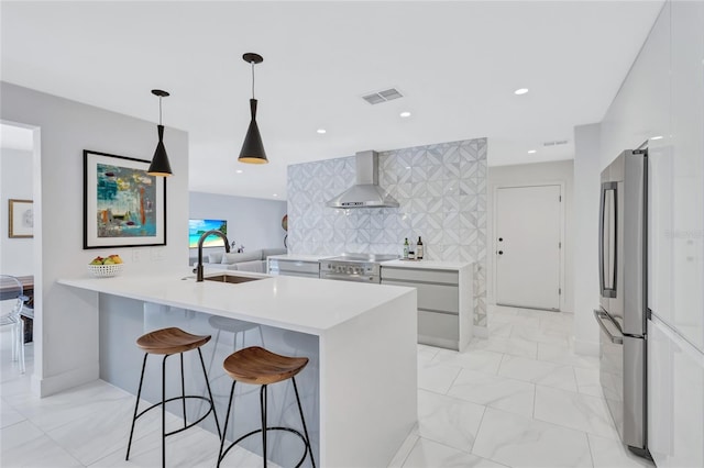 kitchen featuring decorative backsplash, stainless steel appliances, sink, wall chimney range hood, and decorative light fixtures