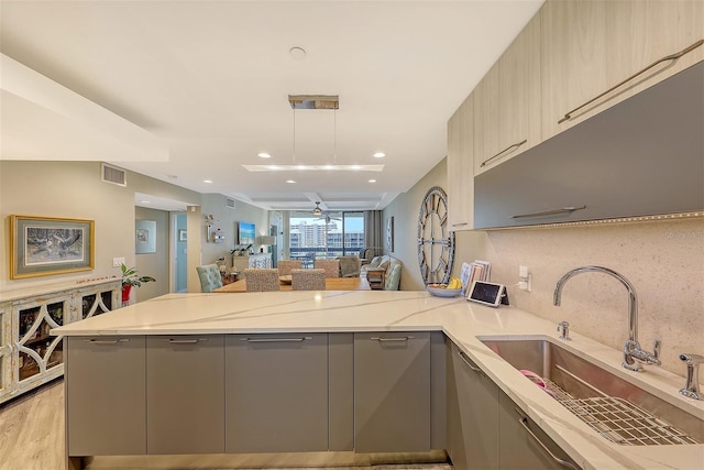 kitchen featuring gray cabinets, light hardwood / wood-style floors, light stone counters, sink, and decorative light fixtures