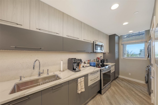 kitchen with stainless steel appliances, light stone countertops, light hardwood / wood-style floors, and sink