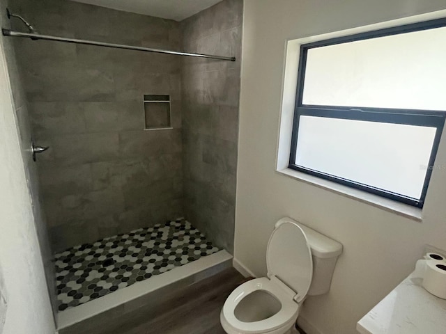 bathroom with tiled shower, wood-type flooring, and toilet