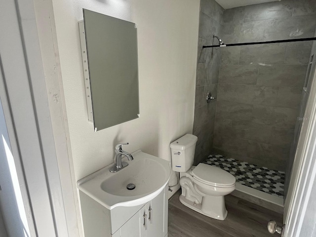 bathroom featuring hardwood / wood-style floors, vanity, toilet, and a tile shower