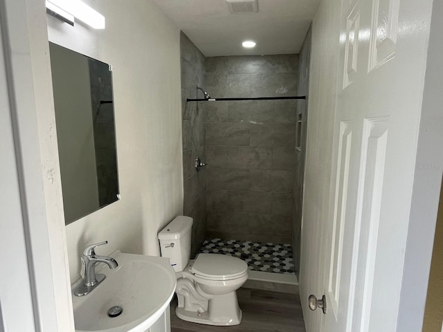 bathroom with a tile shower, sink, wood-type flooring, and toilet