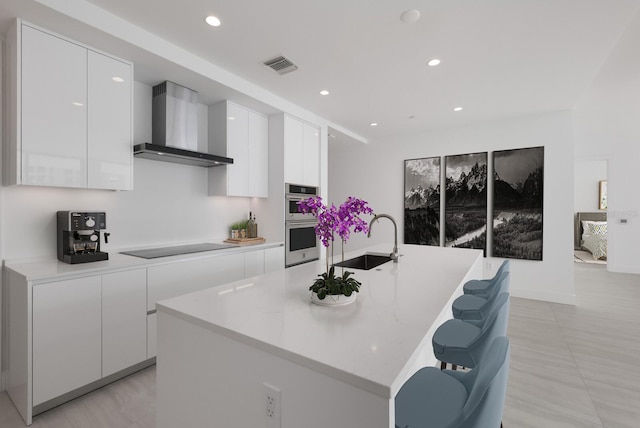 kitchen with white cabinetry, an island with sink, and wall chimney range hood