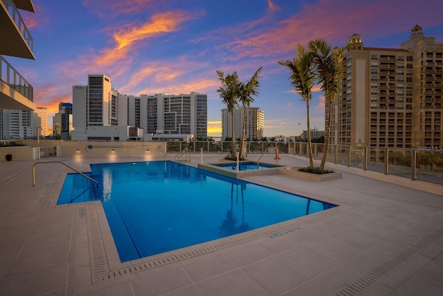 pool at dusk with a patio and a hot tub