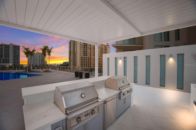 patio terrace at dusk with a fenced in pool, area for grilling, and grilling area