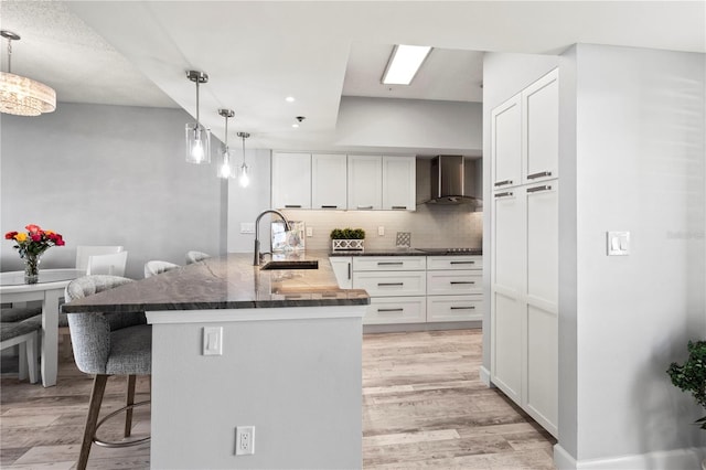 kitchen with pendant lighting, sink, wall chimney exhaust hood, a kitchen bar, and white cabinetry