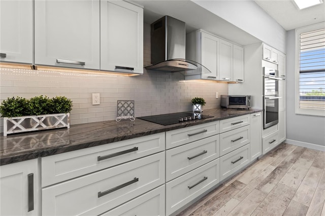 kitchen with wall chimney exhaust hood, white cabinetry, black electric cooktop, and light hardwood / wood-style flooring