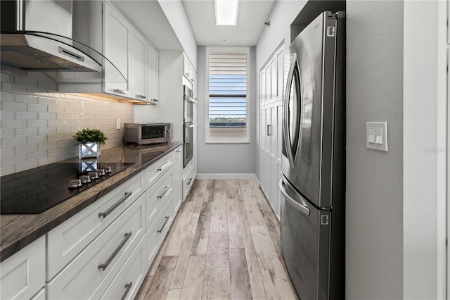 kitchen with wall chimney range hood, decorative backsplash, light wood-type flooring, white cabinetry, and stainless steel appliances