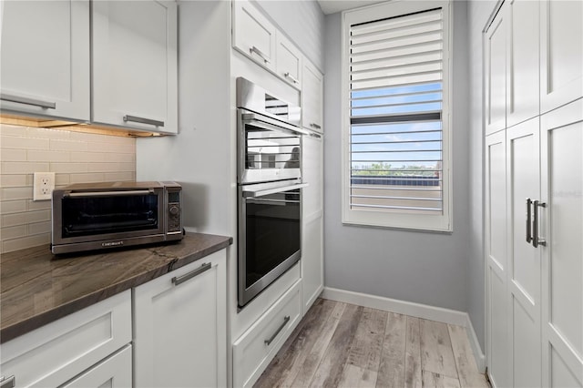 kitchen featuring white cabinetry, light hardwood / wood-style flooring, double oven, and tasteful backsplash