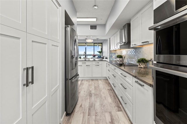 kitchen featuring white cabinets, wall chimney exhaust hood, stainless steel appliances, and light hardwood / wood-style flooring