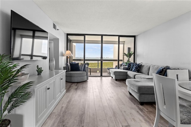 living room with light wood-type flooring, a wall of windows, a textured ceiling, and a wealth of natural light