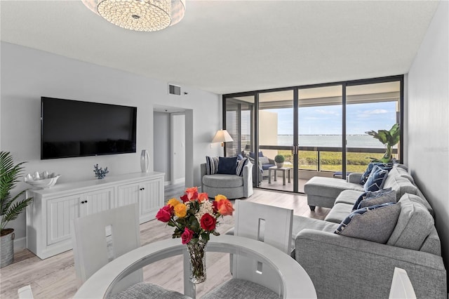 living room featuring light hardwood / wood-style floors, an inviting chandelier, floor to ceiling windows, and a water view