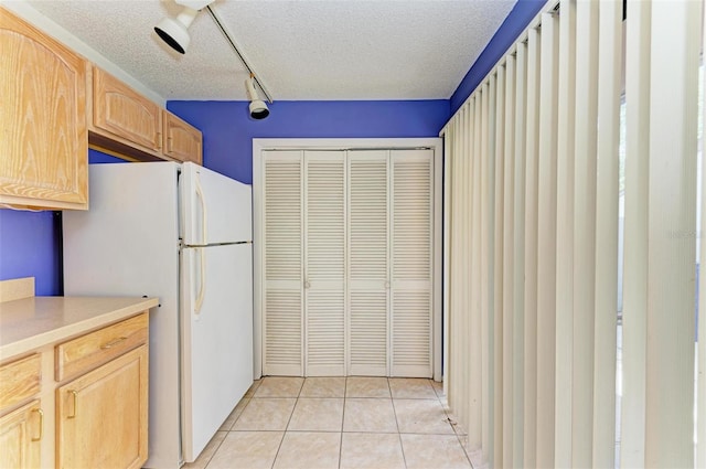 kitchen with white refrigerator, light tile patterned floors, a textured ceiling, and light brown cabinets