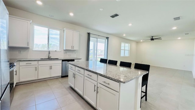 kitchen with sink, a kitchen island, a breakfast bar, white cabinets, and appliances with stainless steel finishes