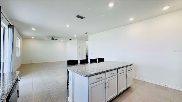 kitchen featuring light stone countertops, ceiling fan, light tile patterned floors, a kitchen island, and white cabinets