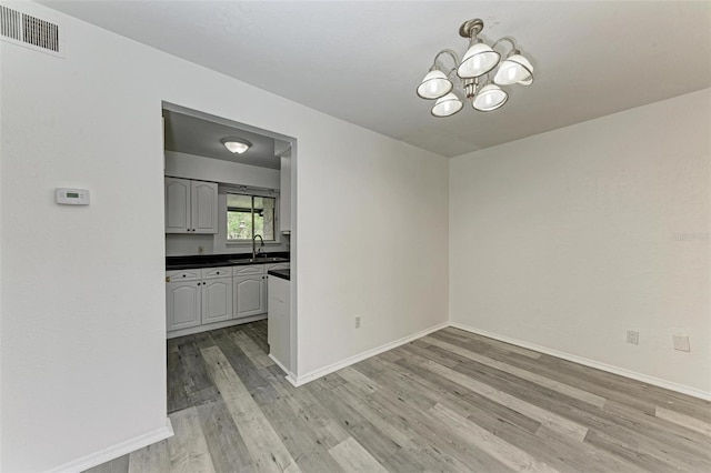 unfurnished dining area featuring sink, an inviting chandelier, and light wood-type flooring