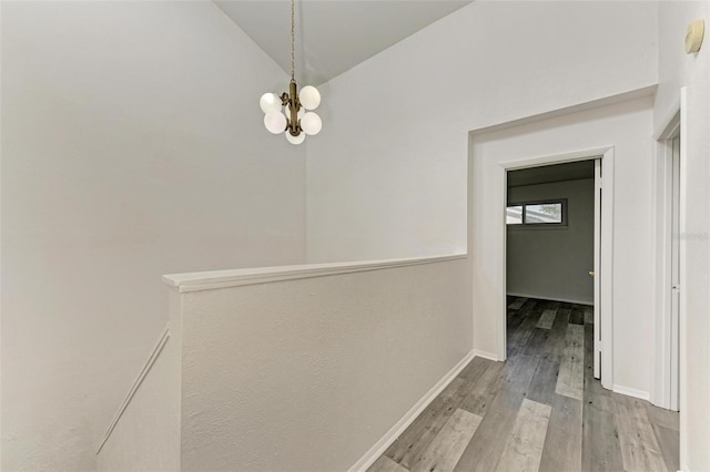 hallway with a notable chandelier, light hardwood / wood-style floors, and high vaulted ceiling