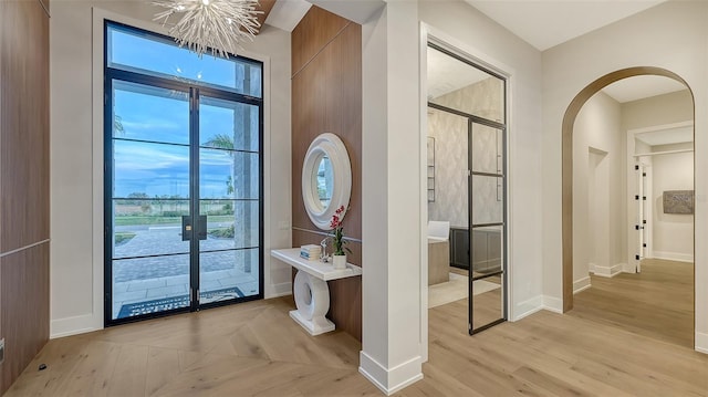 doorway to outside with french doors, light hardwood / wood-style floors, a healthy amount of sunlight, and a notable chandelier