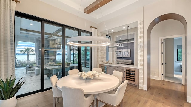 dining space featuring a raised ceiling, wine cooler, and light wood-type flooring