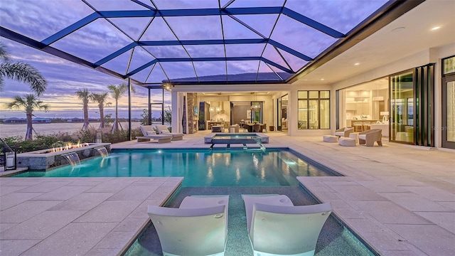 pool at dusk with glass enclosure, pool water feature, a patio area, and an in ground hot tub