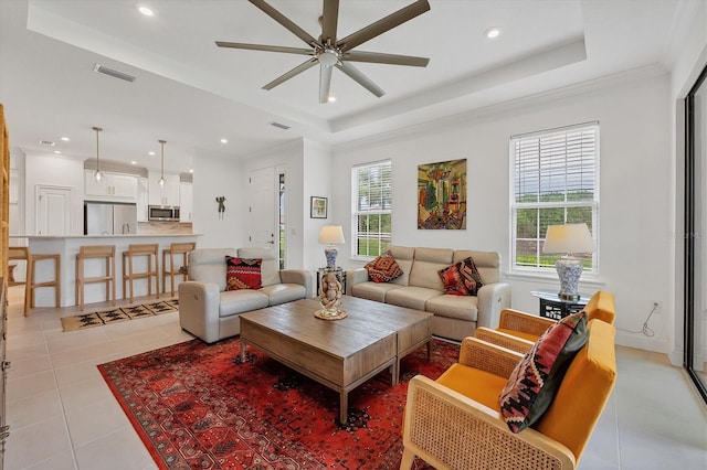 tiled living room with ceiling fan, a raised ceiling, and ornamental molding